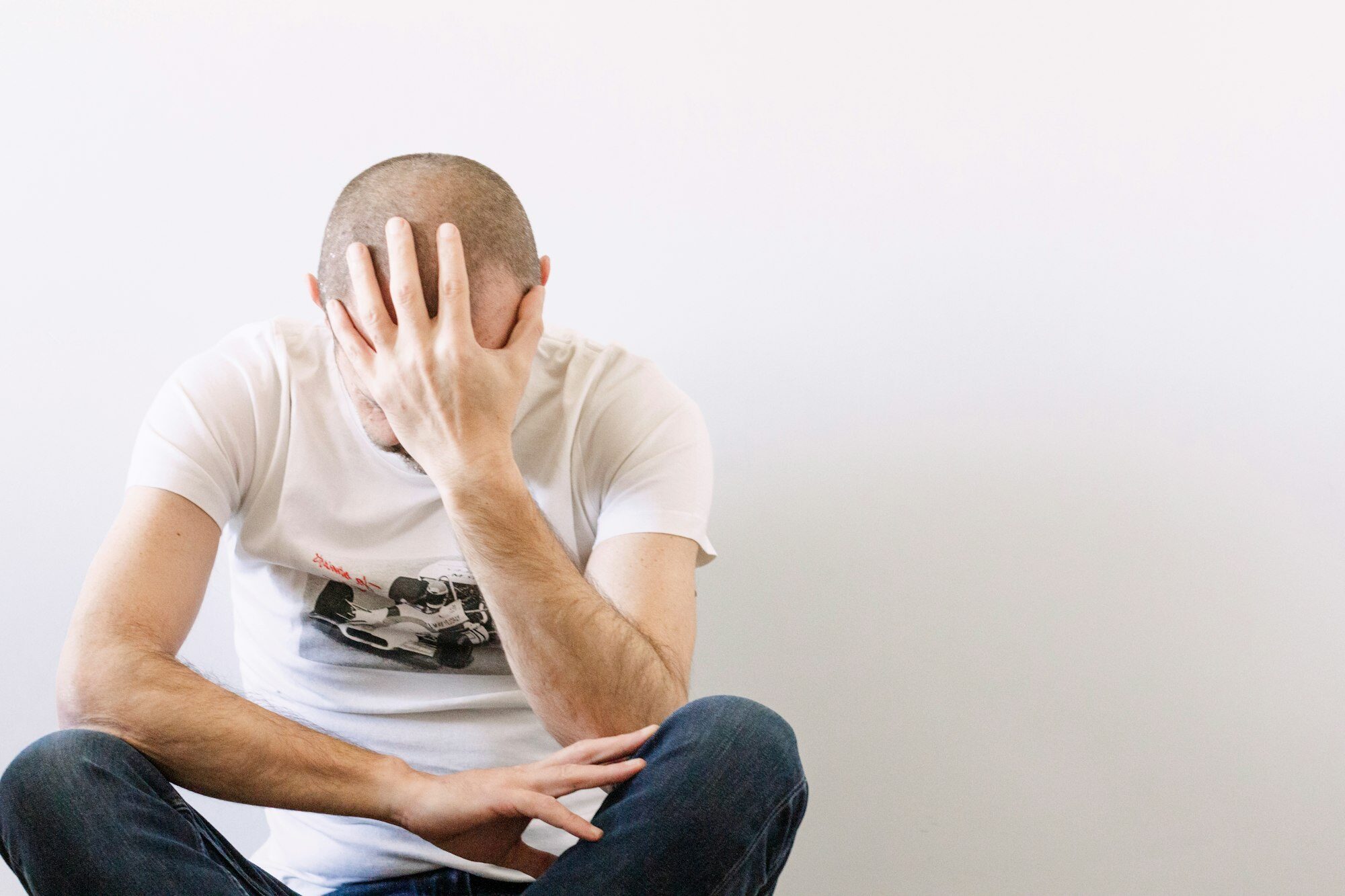 Man looking depressed with a hand on head sitting on the floor