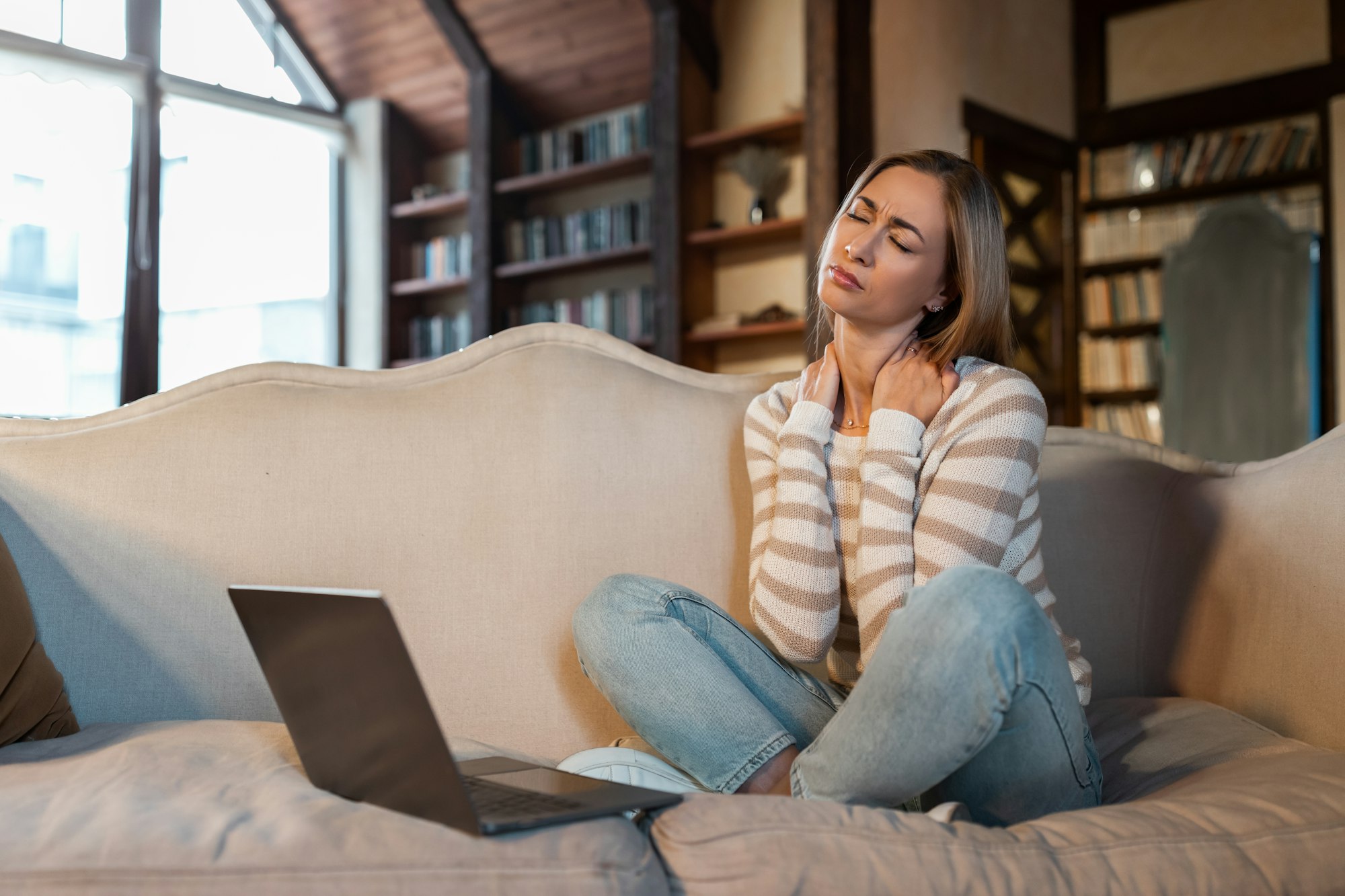 Tired woman sitting on couch with pc, massaging neck