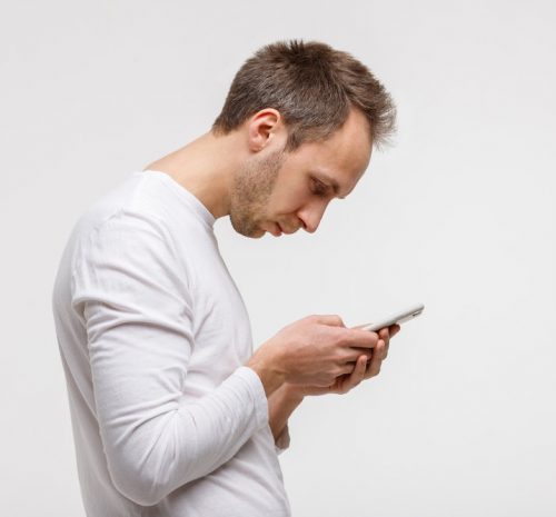 Close up portrait of man looking and using smart phone with scoliosis, side view, isolated on gray background. Rachiocampsis, kyphosis curvature of neck, Incorrect posture,
orthopedics concept